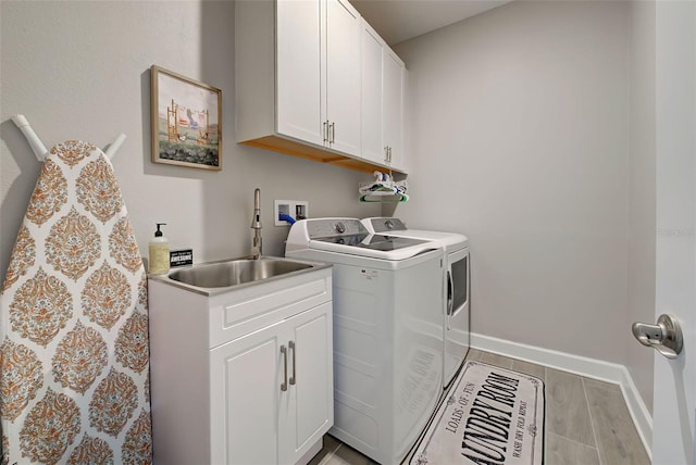 laundry room with washing machine and dryer, sink, cabinets, and light hardwood / wood-style flooring