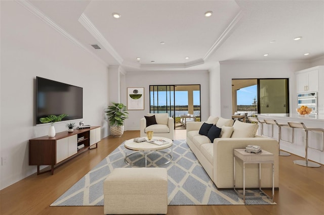 living room featuring crown molding, light hardwood / wood-style floors, and a tray ceiling