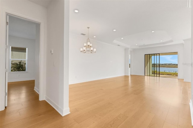 empty room with light wood-type flooring, a notable chandelier, a tray ceiling, recessed lighting, and baseboards