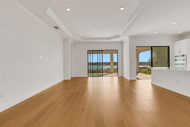 empty room with a tray ceiling, light wood-style flooring, baseboards, and visible vents