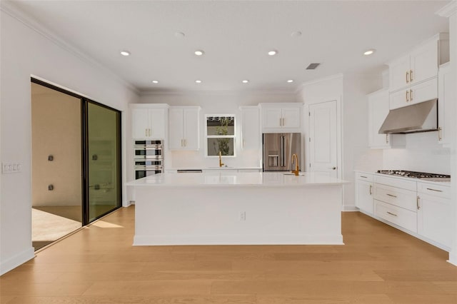 kitchen featuring under cabinet range hood, a large island with sink, appliances with stainless steel finishes, light wood-style floors, and white cabinetry