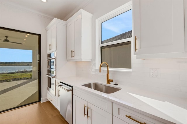 kitchen featuring a sink, backsplash, appliances with stainless steel finishes, white cabinets, and light stone countertops