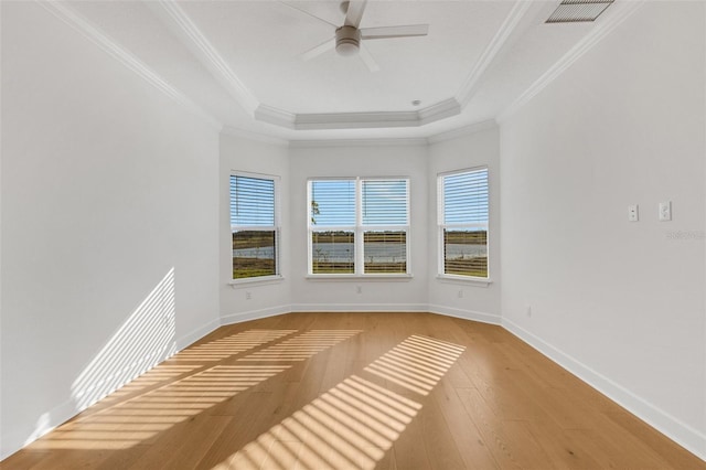 empty room featuring visible vents, a tray ceiling, ornamental molding, a ceiling fan, and wood-type flooring