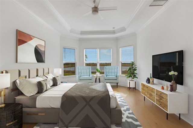 bedroom with a ceiling fan, visible vents, light wood finished floors, a tray ceiling, and crown molding