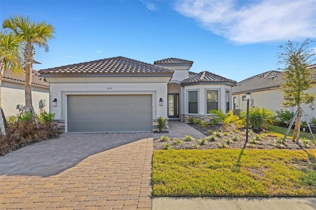 mediterranean / spanish home featuring an attached garage, a tile roof, decorative driveway, and stucco siding