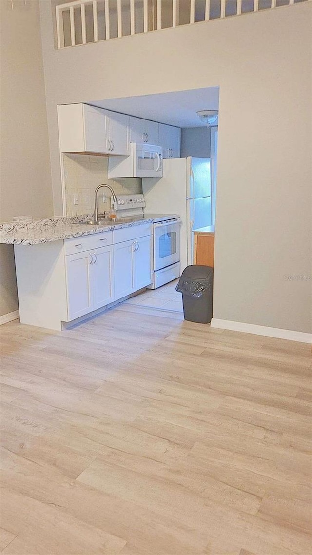 kitchen with light stone counters, white appliances, sink, light hardwood / wood-style flooring, and white cabinetry