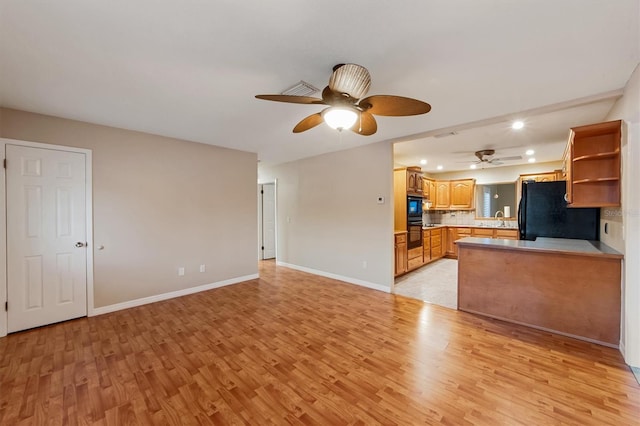 kitchen featuring kitchen peninsula, tasteful backsplash, sink, black appliances, and light hardwood / wood-style floors