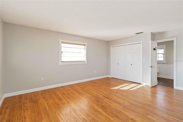 unfurnished bedroom featuring a textured ceiling, a closet, hardwood / wood-style flooring, and multiple windows