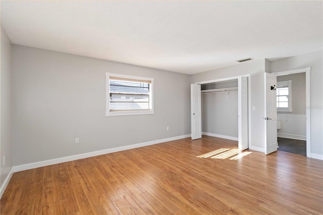 unfurnished bedroom featuring multiple windows, a closet, and hardwood / wood-style flooring