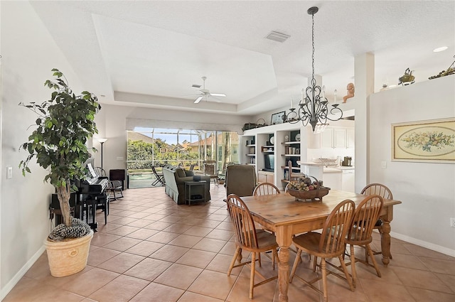 tiled dining room featuring a textured ceiling, ceiling fan with notable chandelier, and a raised ceiling