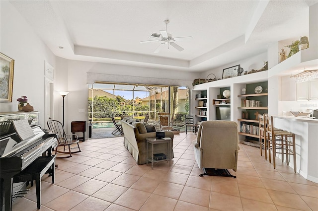 living room featuring a tray ceiling, ceiling fan, and light tile patterned floors