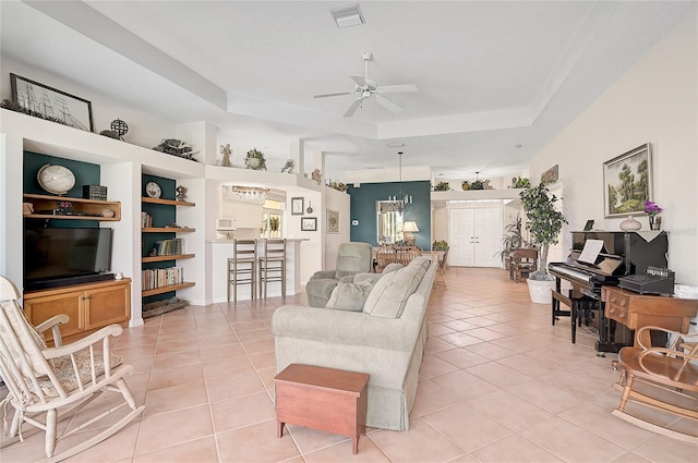 tiled living room with a raised ceiling and ceiling fan with notable chandelier