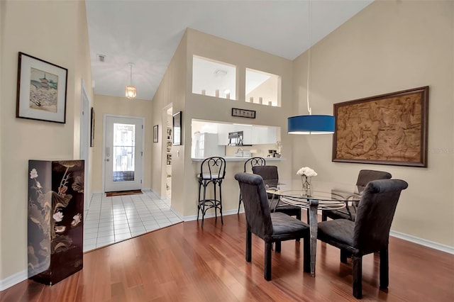 dining room with high vaulted ceiling and light hardwood / wood-style flooring