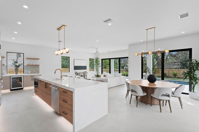 kitchen with an island with sink, sink, pendant lighting, and wine cooler