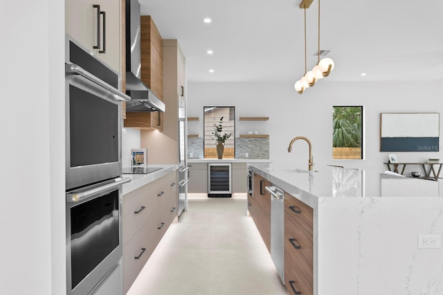 kitchen with appliances with stainless steel finishes, an island with sink, pendant lighting, beverage cooler, and wall chimney range hood