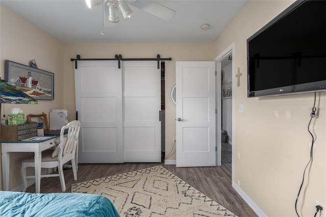 bedroom featuring a barn door, ceiling fan, and dark wood-type flooring