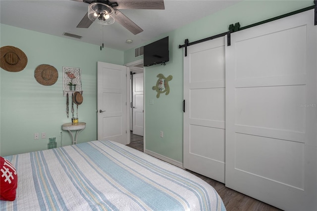 bedroom featuring hardwood / wood-style floors, ensuite bath, ceiling fan, a barn door, and a closet