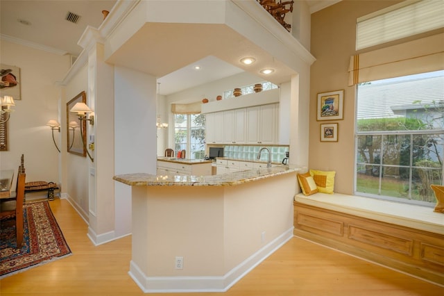 kitchen with kitchen peninsula, light hardwood / wood-style flooring, light stone countertops, ornamental molding, and white cabinetry