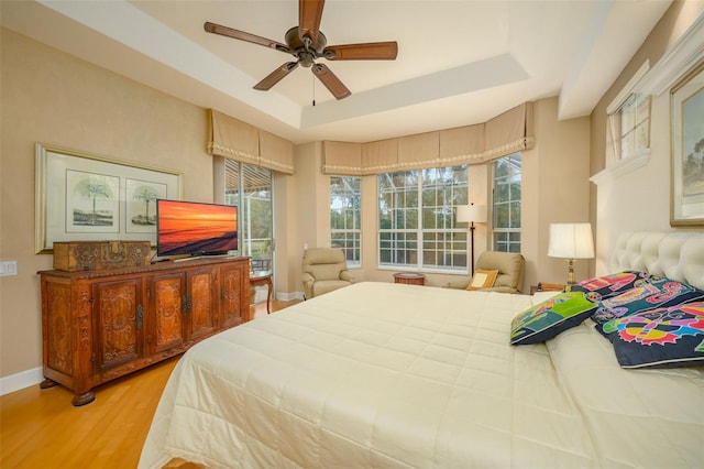 bedroom featuring light hardwood / wood-style flooring, a raised ceiling, and ceiling fan