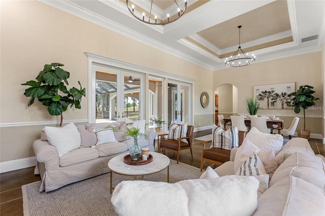 living room featuring arched walkways, a chandelier, baseboards, ornamental molding, and a raised ceiling