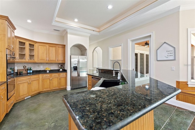 kitchen featuring stainless steel appliances, tasteful backsplash, a raised ceiling, a sink, and a large island with sink