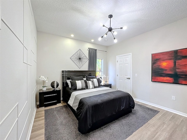 bedroom with an inviting chandelier, a textured ceiling, and light wood-type flooring