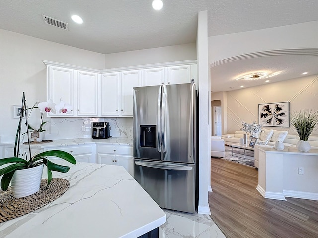 kitchen with white cabinetry, stainless steel fridge, backsplash, light stone counters, and a textured ceiling