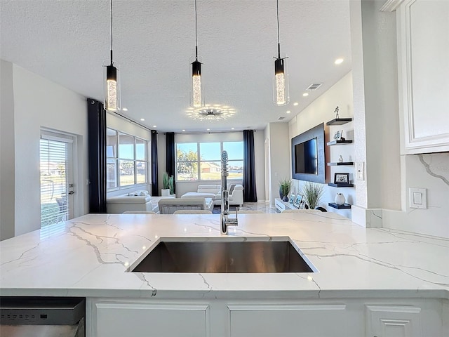 kitchen featuring light stone counters, hanging light fixtures, sink, and a textured ceiling