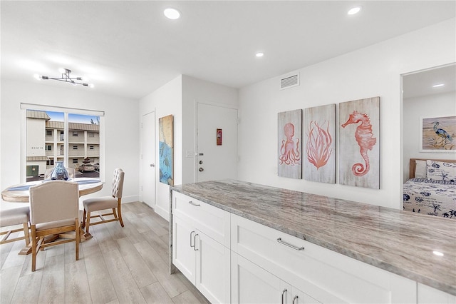 kitchen with light stone counters, white cabinets, and light wood-type flooring