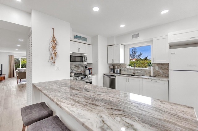 kitchen featuring a breakfast bar area, stainless steel appliances, light stone countertops, white cabinets, and sink