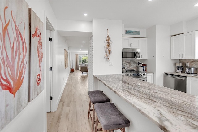 kitchen featuring a breakfast bar area, backsplash, appliances with stainless steel finishes, and white cabinetry