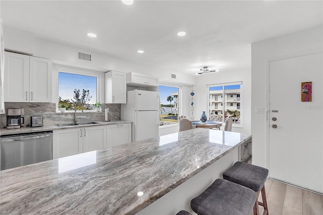 kitchen with light stone countertops, white cabinets, dishwasher, white refrigerator, and sink