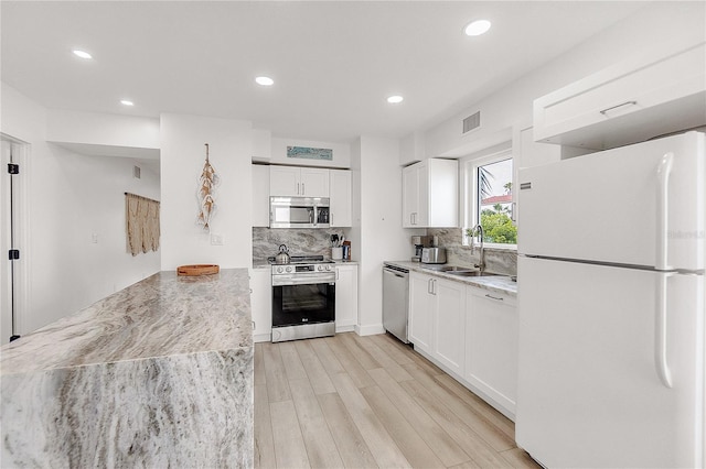 kitchen with white cabinetry, appliances with stainless steel finishes, backsplash, light stone counters, and sink