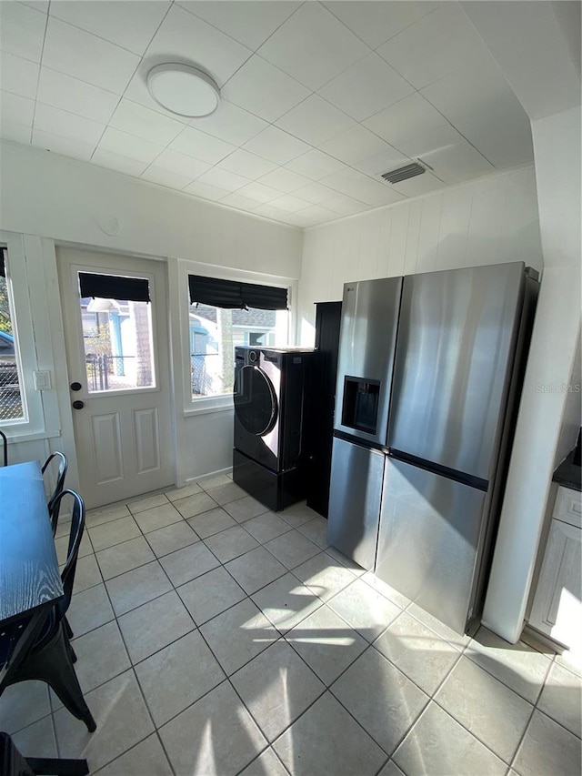 kitchen with stainless steel fridge with ice dispenser, light tile patterned floors, and washer / dryer