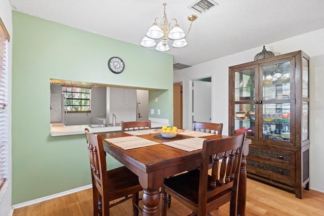 dining room featuring sink, light hardwood / wood-style flooring, a textured ceiling, and an inviting chandelier