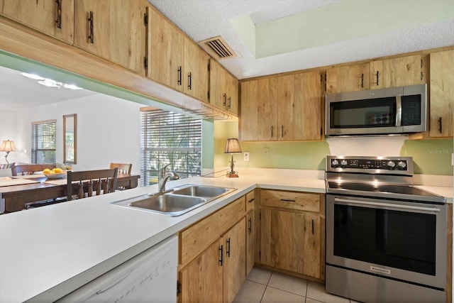 kitchen with sink, light tile patterned floors, a textured ceiling, light brown cabinetry, and appliances with stainless steel finishes