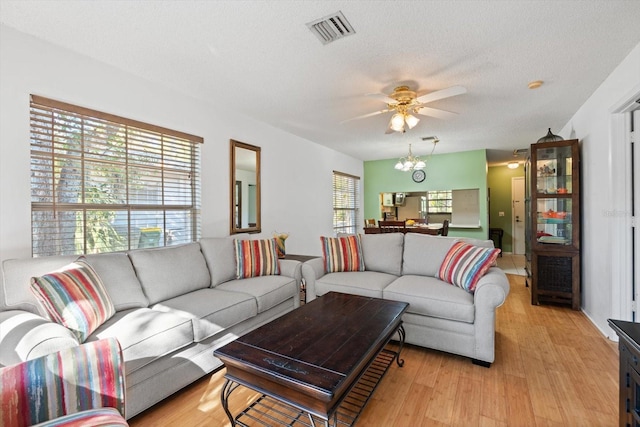 living room featuring ceiling fan with notable chandelier, a textured ceiling, and light hardwood / wood-style flooring