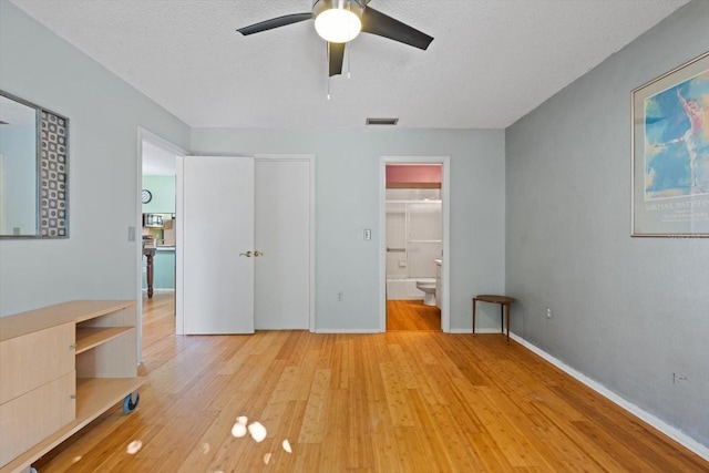 unfurnished bedroom with a textured ceiling, light wood-type flooring, ensuite bath, and ceiling fan