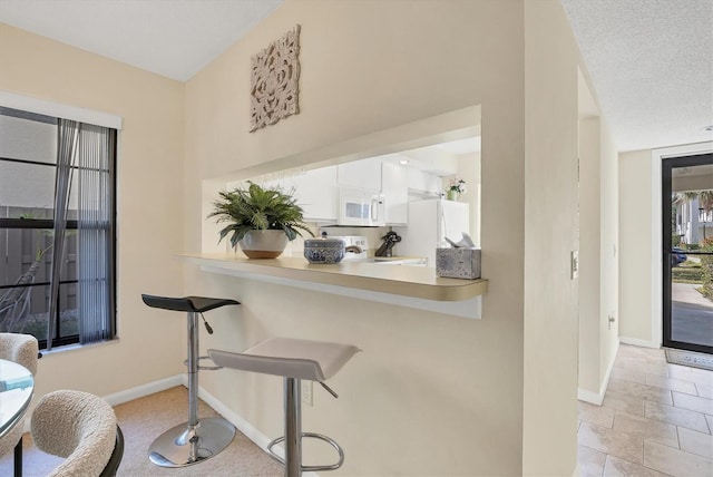 kitchen featuring white cabinets, kitchen peninsula, white appliances, and a textured ceiling