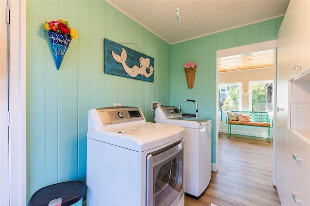 clothes washing area with washing machine and clothes dryer, wood walls, and light hardwood / wood-style floors