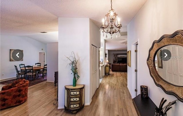 hallway with a notable chandelier, light wood-type flooring, and a textured ceiling