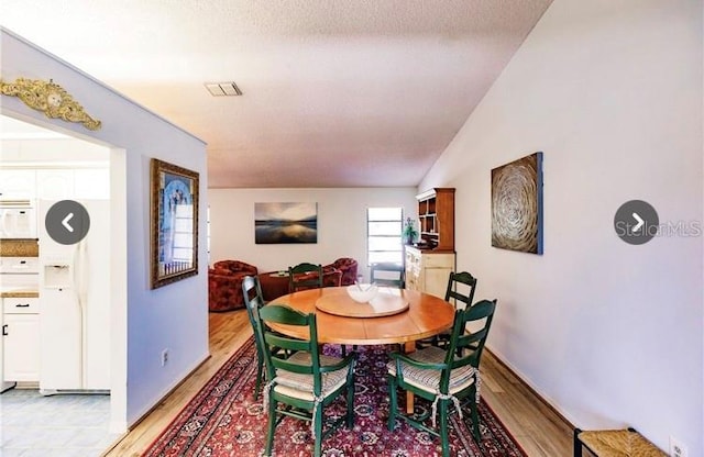 dining area with vaulted ceiling, a textured ceiling, and light hardwood / wood-style flooring