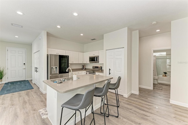 kitchen with white cabinets, a center island with sink, sink, appliances with stainless steel finishes, and light hardwood / wood-style floors