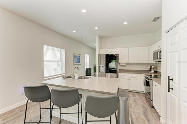 kitchen featuring light wood-type flooring, stainless steel appliances, sink, white cabinets, and an island with sink