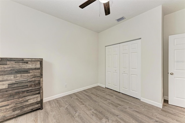 unfurnished bedroom with ceiling fan, a closet, light hardwood / wood-style floors, and a textured ceiling