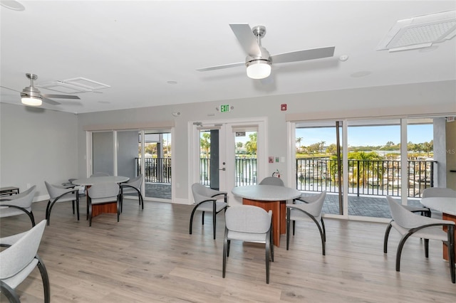 dining area with ceiling fan, french doors, a water view, and light wood-type flooring