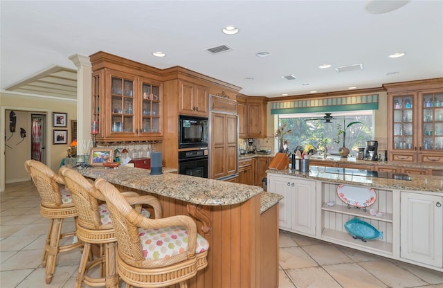 kitchen with a kitchen bar, kitchen peninsula, light stone counters, black appliances, and white cabinetry