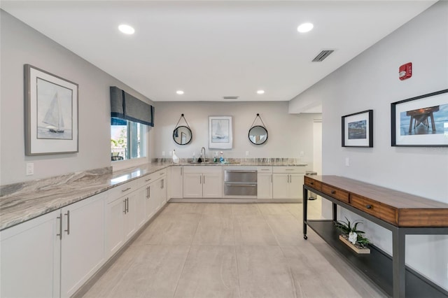 kitchen featuring kitchen peninsula, white cabinetry, sink, and light stone countertops