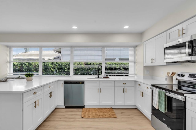 kitchen with appliances with stainless steel finishes, light hardwood / wood-style floors, white cabinetry, and sink