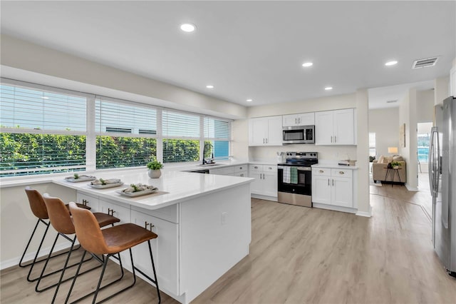 kitchen featuring a kitchen bar, appliances with stainless steel finishes, light wood-type flooring, sink, and white cabinets